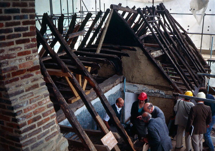 ancient roof timbers under tarpaulin, people in hard hats